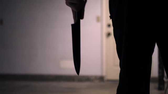 A scary slasher killer holding a kitchen knife in silhouette and walking towards his murder victim in a home invasion SLOW MOTION.
