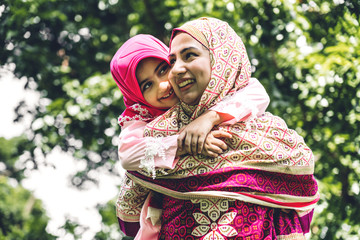 Portrait of happy lovely family arabic muslim mother and little muslim girls child with hijab dress smiling and having fun hugging and kissing together in summer park