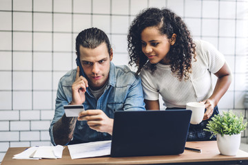 Happy smiling couple relaxing and shopping online with technology of laptop computer and credit card together sitting in living room at home