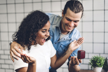 Young handsome man giving ring for surprise to girlfriend and talking together sitting in living room at home