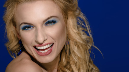 Young beautiful blonde with curly hair posing and smiling on blue background