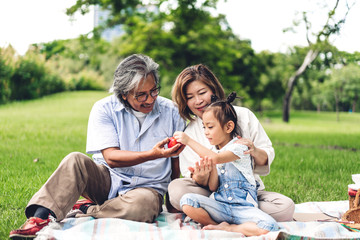 Portrait of happy grandfather with grandmother and little cute girl enjoy relax in summer park.Young girl with their laughing grandparents smiling together.Family and togetherness