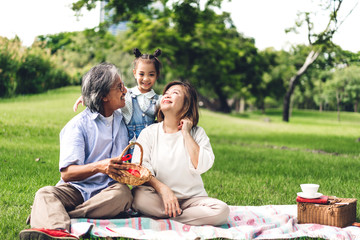 Portrait of happy grandfather with grandmother and little cute girl enjoy relax in summer park.Young girl with their laughing grandparents smiling together.Family and togetherness