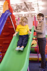 Grandson and grandmother riding on a hill. Portrait of a blond boy in a yellow t-shirt. The child smiles and plays in the children's playroom.