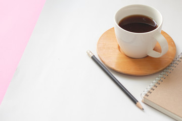 Cup of coffee with pencil and notebook on white and pink background.