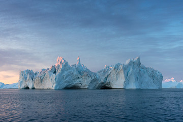 Fototapeta na wymiar Iceberg at sunset. Nature and landscapes of Greenland. Disko bay. West Greenland. Summer Midnight Sun and icebergs. Big blue ice in icefjord. Affected by climate change and global warming.