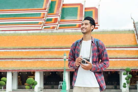 Asian Man Tourist Walk Taking Photo With Film Camera  At Wat Suthat Thepwararam Ratchaworawihan Bangkok, Thailand In The Summer Time, Solo Travel And Backpacker Concept