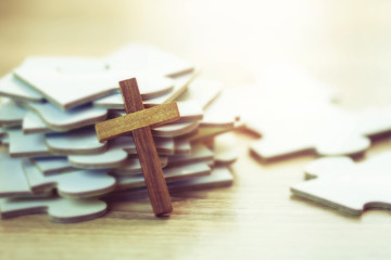 Close up of wooden cross over white jigsaw puzzle on wooden desk background, Christian concept show Jesus is the most important piece in human life, copy space