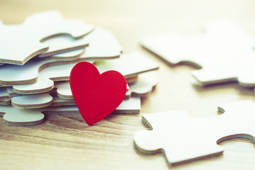 Plakat Red heart over pile of jigsaws on wooden table, Conceptual image show most important part of human life is love