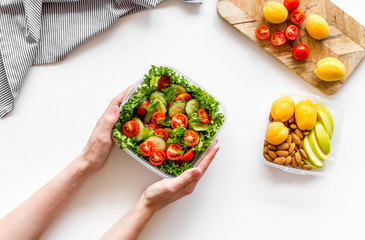 Food container with healthy food in hands on white background top view