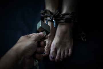 Close up of a man hand hold the key while try to unlock on metal padlock which bondage on woman's legs to help and release her from suffering. sex abuse   prevention concept, copy space