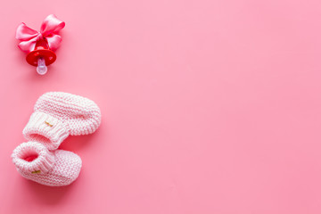 Obraz na płótnie Canvas Pink knitted footwear and dummy for baby on pink background top view mockup