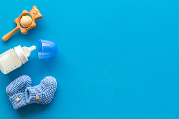 Blue knitted footwear and rattle, bottle for baby on blue background top view mockup