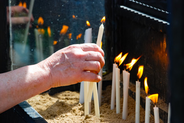 Woman's hand puts the flaming candle with reflection on the glass in the church.