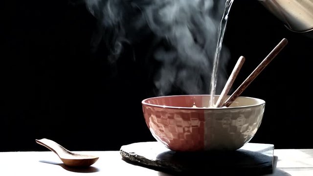 Woman pouring hot water into instant noodles in cup with smoke rising and garlic on dark background, Sodium diet high risk kidney failure, Healthy eating concept