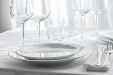 Table setting white and grey colour. Empty glasses and plates set with napkin and cutlery on white table cloth. Restaurant interior background.