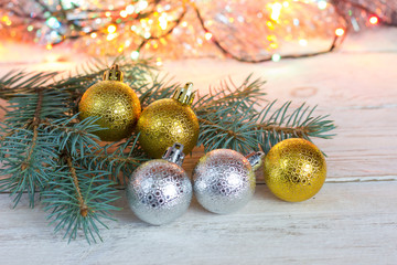 Christmas card. Silver and golden christmas balls on a light wooden table. Fir branch and bokeh in the background.