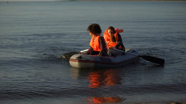 Two women in life jackets rowing boat, flood survivors seeking help ashore