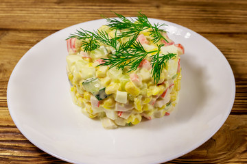Salad with crab sticks, sweet corn, cucumber, eggs and mayonnaise on wooden table