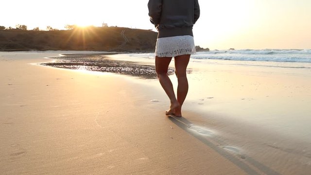 Low angle of young woman walking barefoot on the beach at sunrise