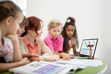 Children discussing final test with their pleasant smiling teacher