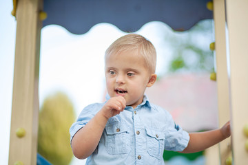 A boy with Down syndrome plays in the playground. Genetic disease in a child.
