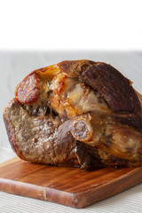 Roasted leg of lamb resting on a wooden chopping board and place mat.  Grey wood background