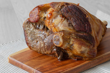 Roasted leg of lamb resting on a wooden chopping board and place mat.  Grey wood background