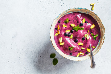 Blueberry smoothie bowl with pistachios and mint on white background, top view. Healthy vegan breakfast.