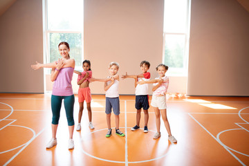 Fototapeta premium PE teacher and children stretching arms before starting physical training
