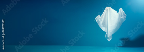 Photo of halloween ghosts made of white fabric on empty blue background.