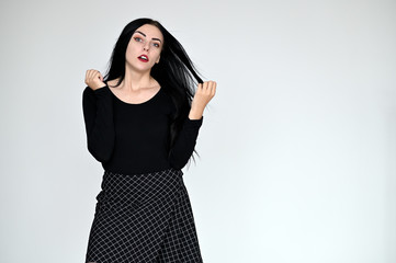 Concept portrait of a pretty brunette girl with long black hair in dark clothes on a white background in studio. Standing right in front of the camera in different poses with different emotions.