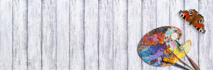 Palette for oil paints with brushes and palette knife and peacock butterfly on shabby wooden table