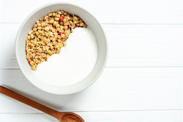 white wheat granola with low-fat yogurt in a white bowl in a composition with a spoon on white wooden background. Healthy breakfast food. Making breakfast. Gluten free