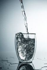 Fresh and cold, pure Water is poured into a glass. Purified water in a glass on a gray background. Motion freeze splash of crystal water on grey background.