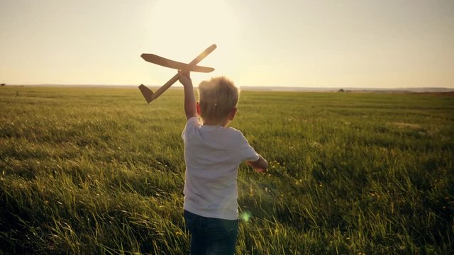 Happy child in a white T-shirt runs with a toy airplane on a sunset background over a field. The concept of a happy family. Childhood dreams