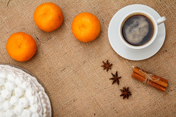 Biscuit cake decorated with whipped cream, cup of coffee, oranges, star anise and cinnamon