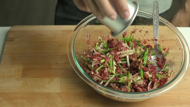 Process of making kimchi. A man pouring fish sauce into kimchi paste mix and stir with a spoon.