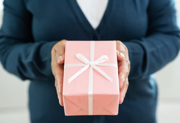 Senior woman in blue sweater is holding a pink gift box