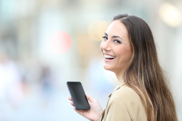 Happy woman holding phone looks at camera in the street