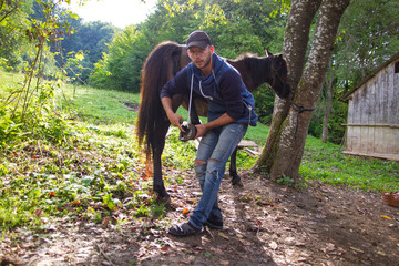 man cleans horse hooves on farm