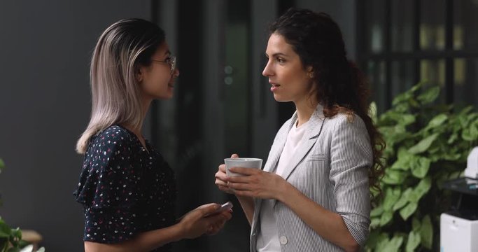 Two happy friendly young diverse business women talking in office