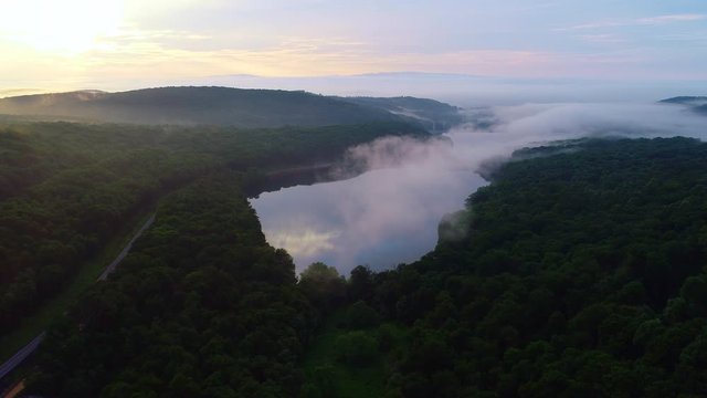 Drone flying forward over a lake and fores during the early morning.  A layer of mist/clouds is hovering over the lake