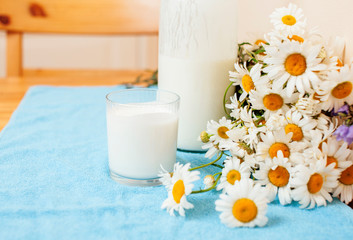 Simply stylish wooden kitchen with bottle of milk and glass on table, summer flowers camomile, healthy foog moring concept