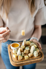 Girl holding piece of parmesan cheese on a skewer and wooden plate with cheese. Delicious cheese mix with walnuts, honey. Food for wine.