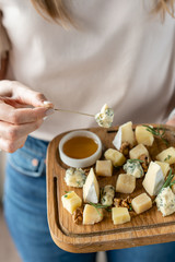 Girl holding piece of Gorgonzola cheese on a skewer and wooden plate with cheese. Delicious cheese mix with walnuts, honey. Food for wine.