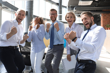 Fototapeta na wymiar Five happy modern business people are keeping arms raised and expressing joyful while standing in large office