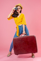 Smiling woman traveler holding camera and luggage in holiday on pink backgrounds, relaxation concept, travel concept