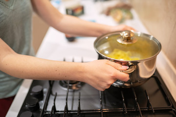 Beautiful young woman housewife prepairing dinner, hold in hands big steel saucepan, standing it on gas-stove.