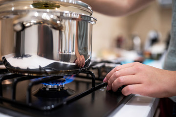 Beautiful young woman housewife prepairing dinner, hold in hands big steel saucepan, standing it on gas-stove.